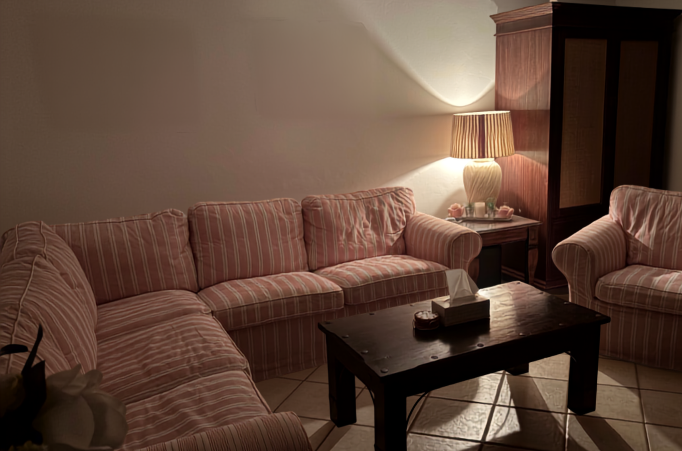 A striped sofa living room in warm evening lamplight beside a dark wood wardrobe