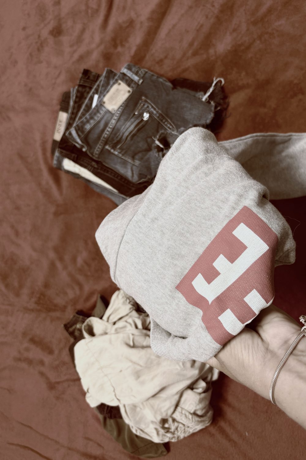A hand holding a folded sweatshirt and jeans while sorting clothes