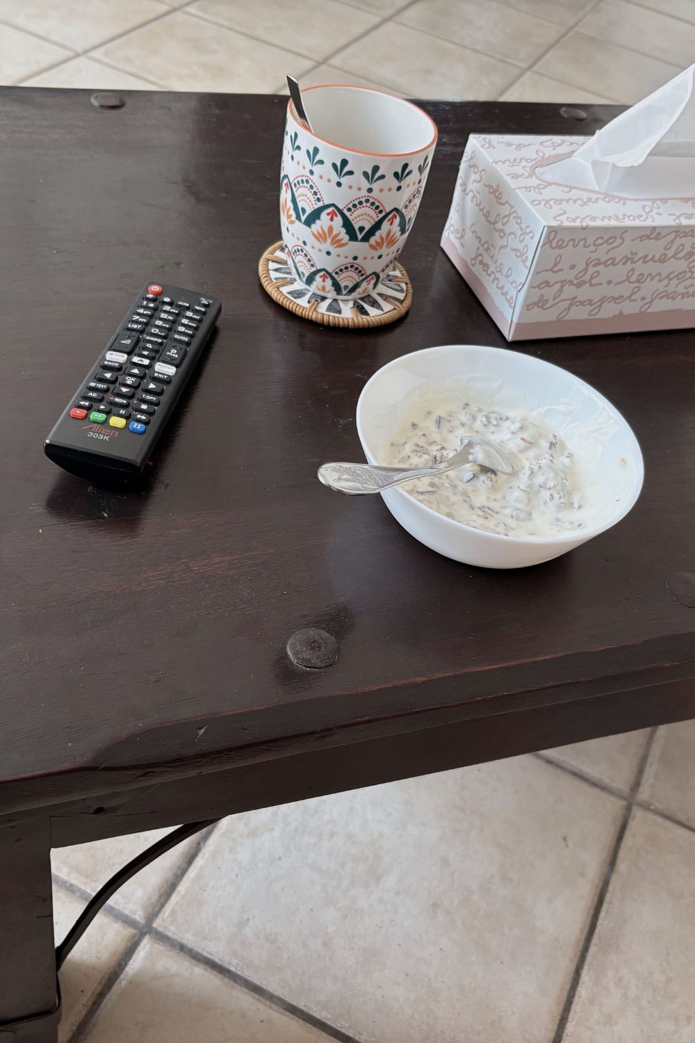 A coffee table with a remote, mug, tissue box and cereal bowl left out
