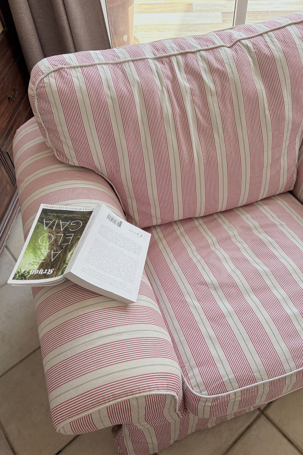 A striped armchair by a window with an open book resting on the arm